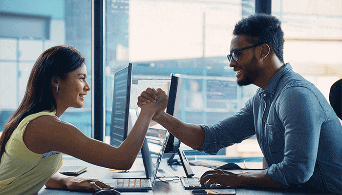 Young lady and male developer working together with computers smiling and fist bumping nice. Modern office vibe.